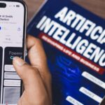 Smartphone displaying AI app with book on AI technology in background.