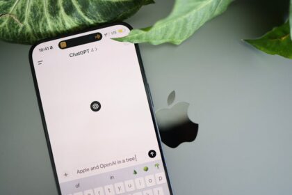 A smartphone shows a ChatGPT interface placed on an Apple laptop in a leafy environment.