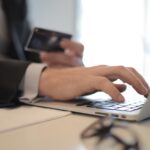 Man in suit using laptop and credit card for online transaction at work.