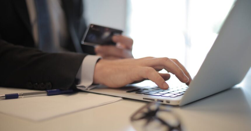 Man in suit using laptop and credit card for online transaction at work.